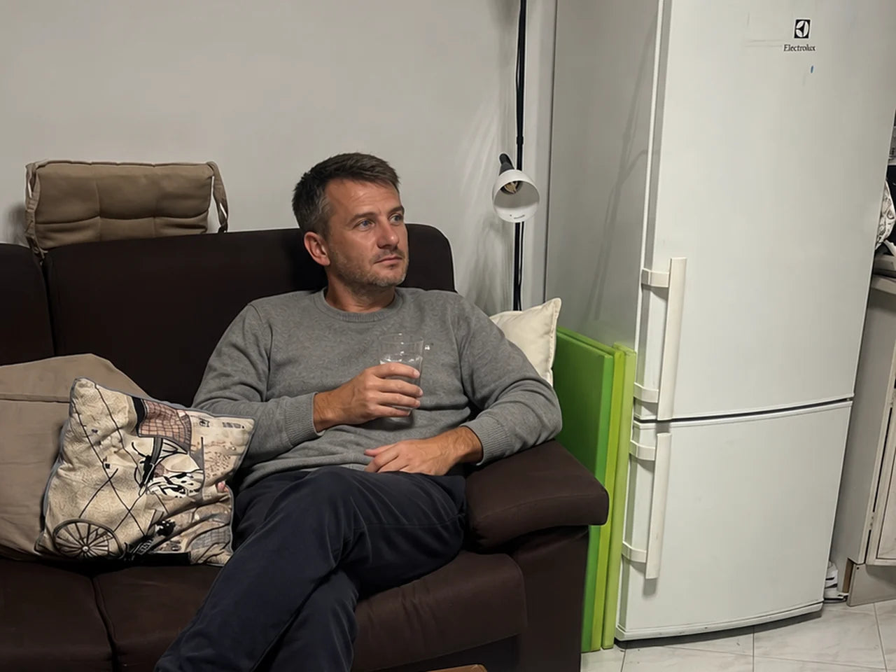 Mann sitzt abends entspannt mit einem Glas auf dem Sofa
