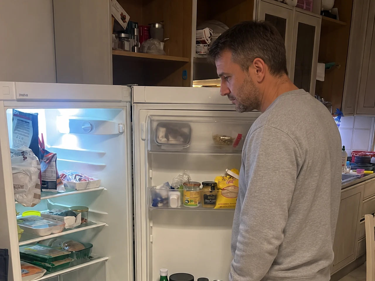 Mann steht spätabends vor dem offenen Kühlschrank